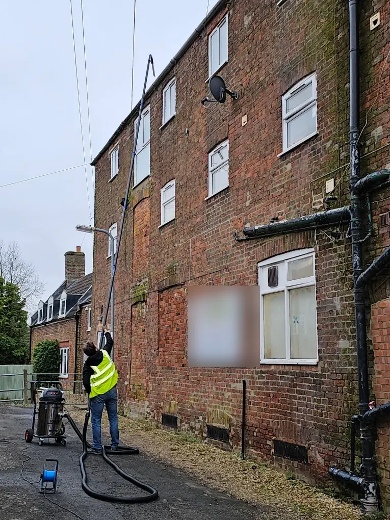 Technician cleaning gutters on a three-storey brick building with a gutter vacuum pole